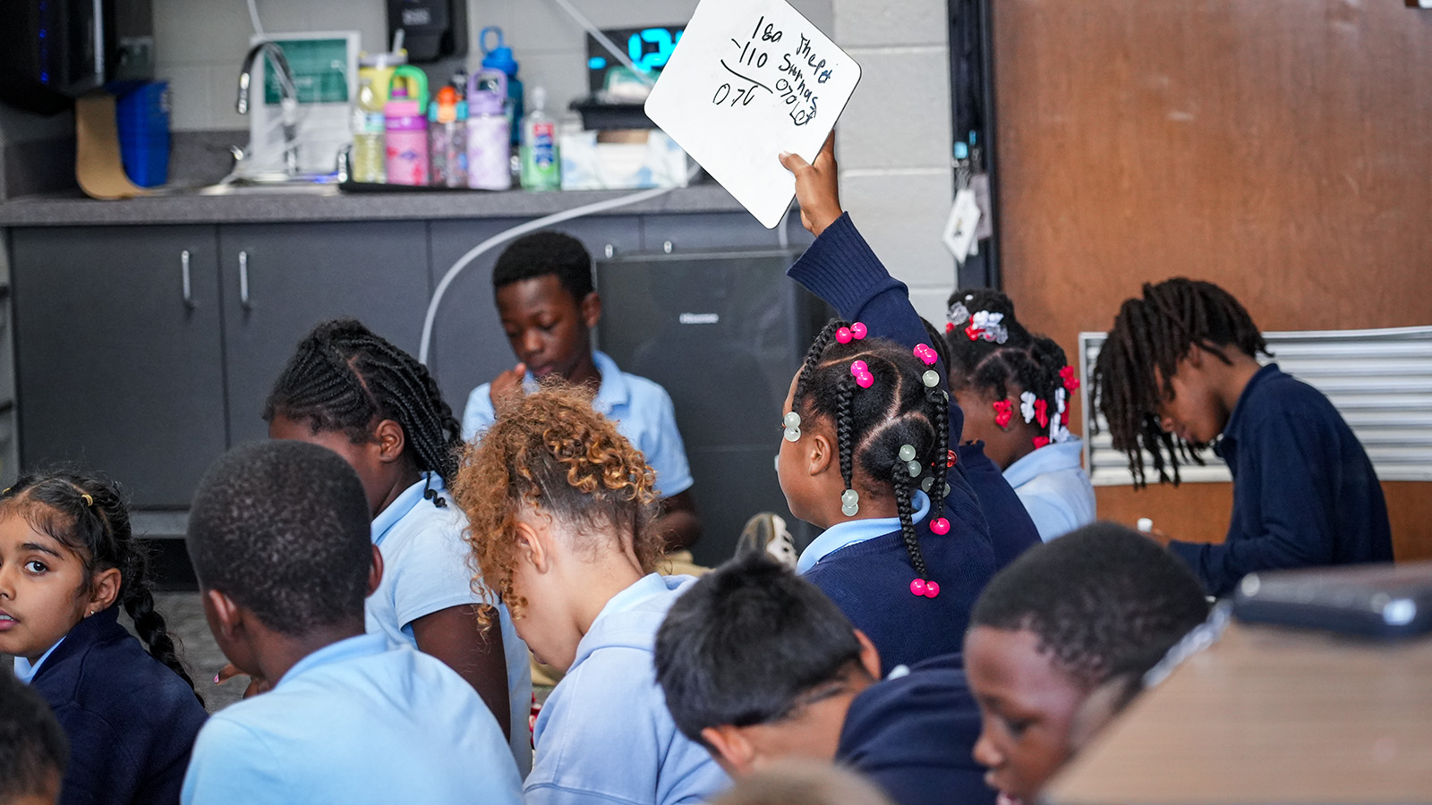 Paramount South Bend students participating in a classroom activity as a student raises a whiteboard to share her work