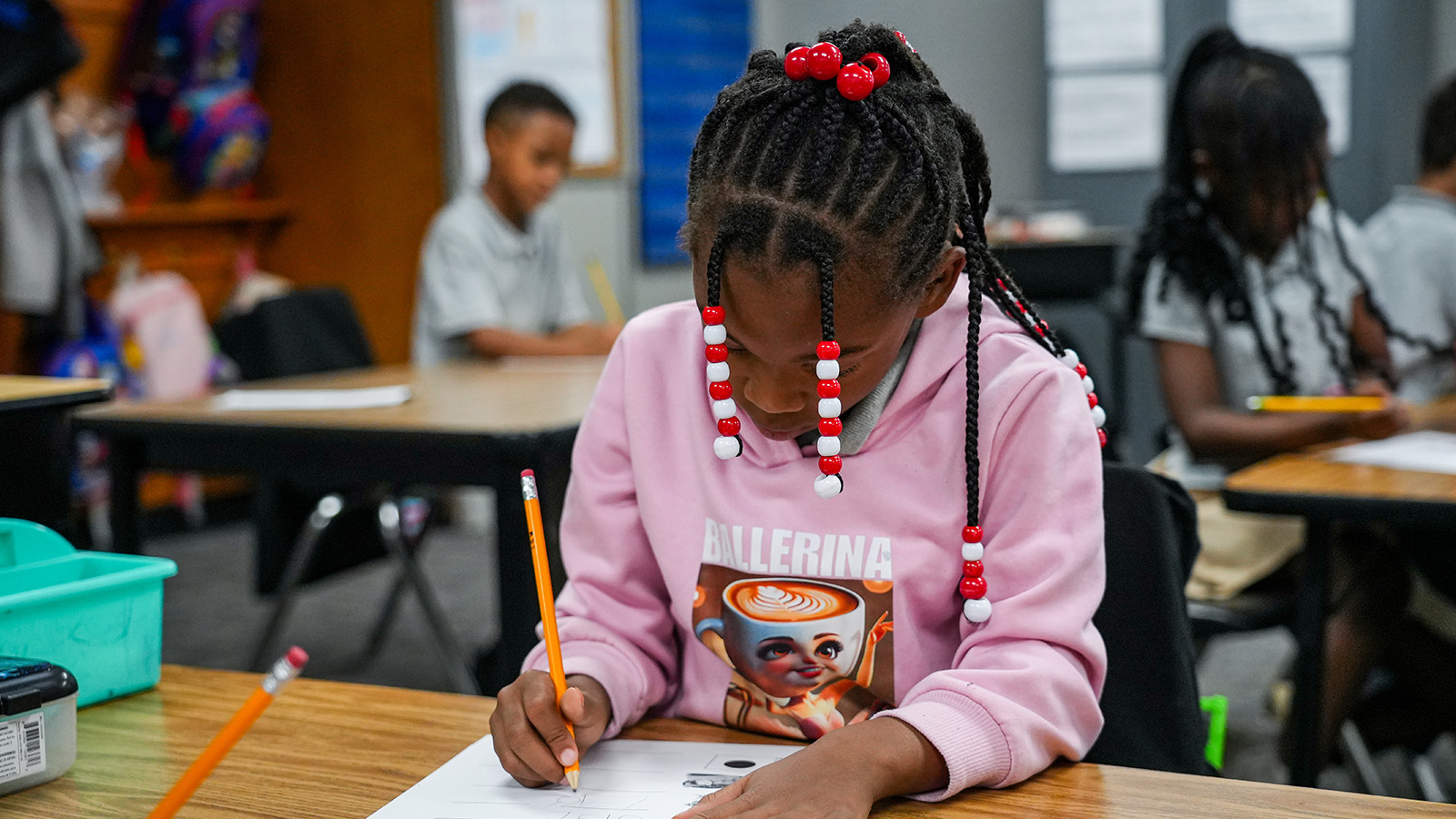 Paramount South Bend student concentrating on a writing assignment at her classroom desk while classmates work in the background