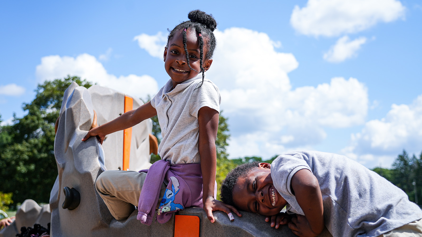 Two smiling Paramount South Bend students climbing and playing together on outdoor playground equipment