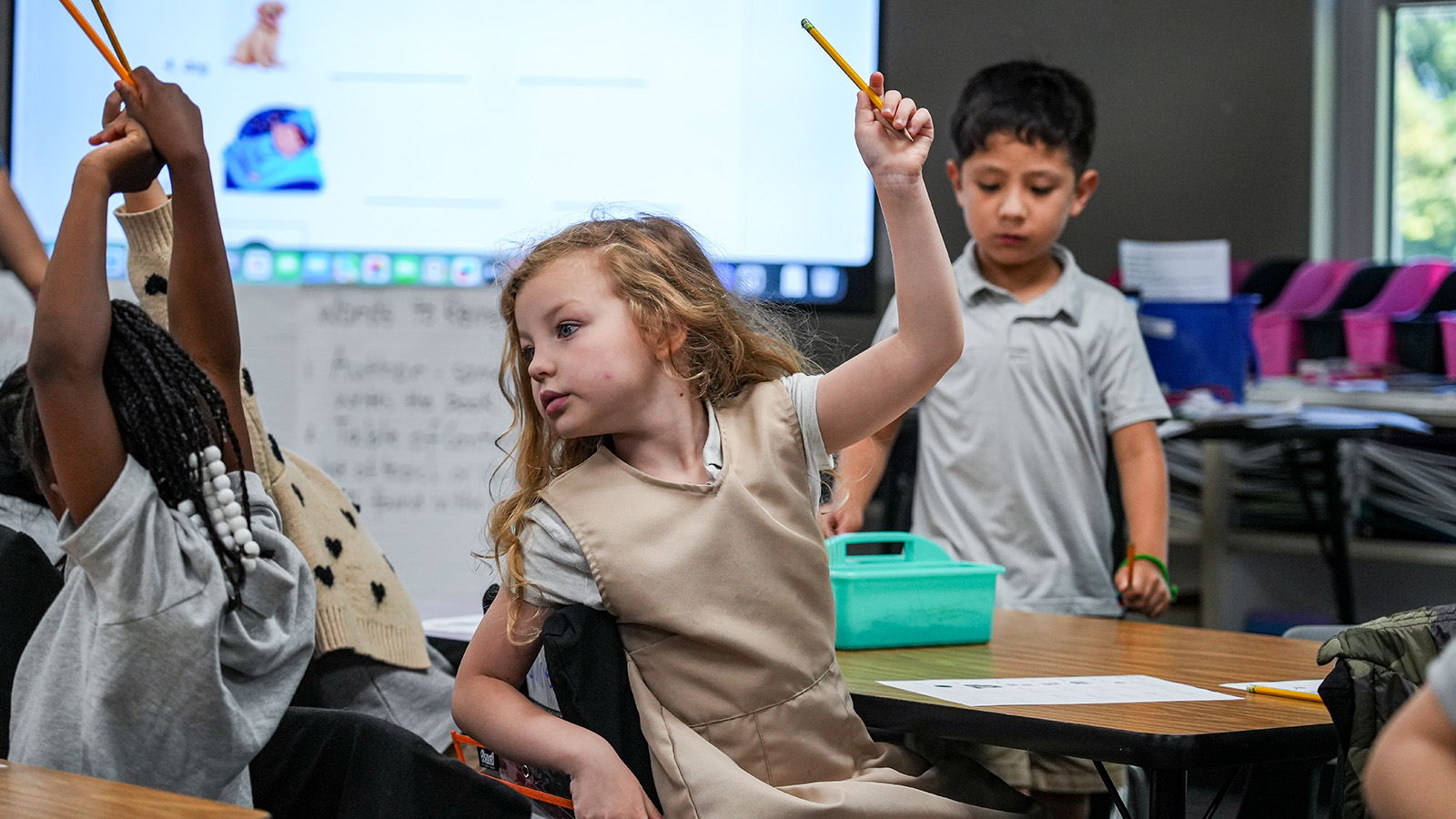 Paramount South Bend student raising her hand while holding a pencil during an interactive classroom lesson
