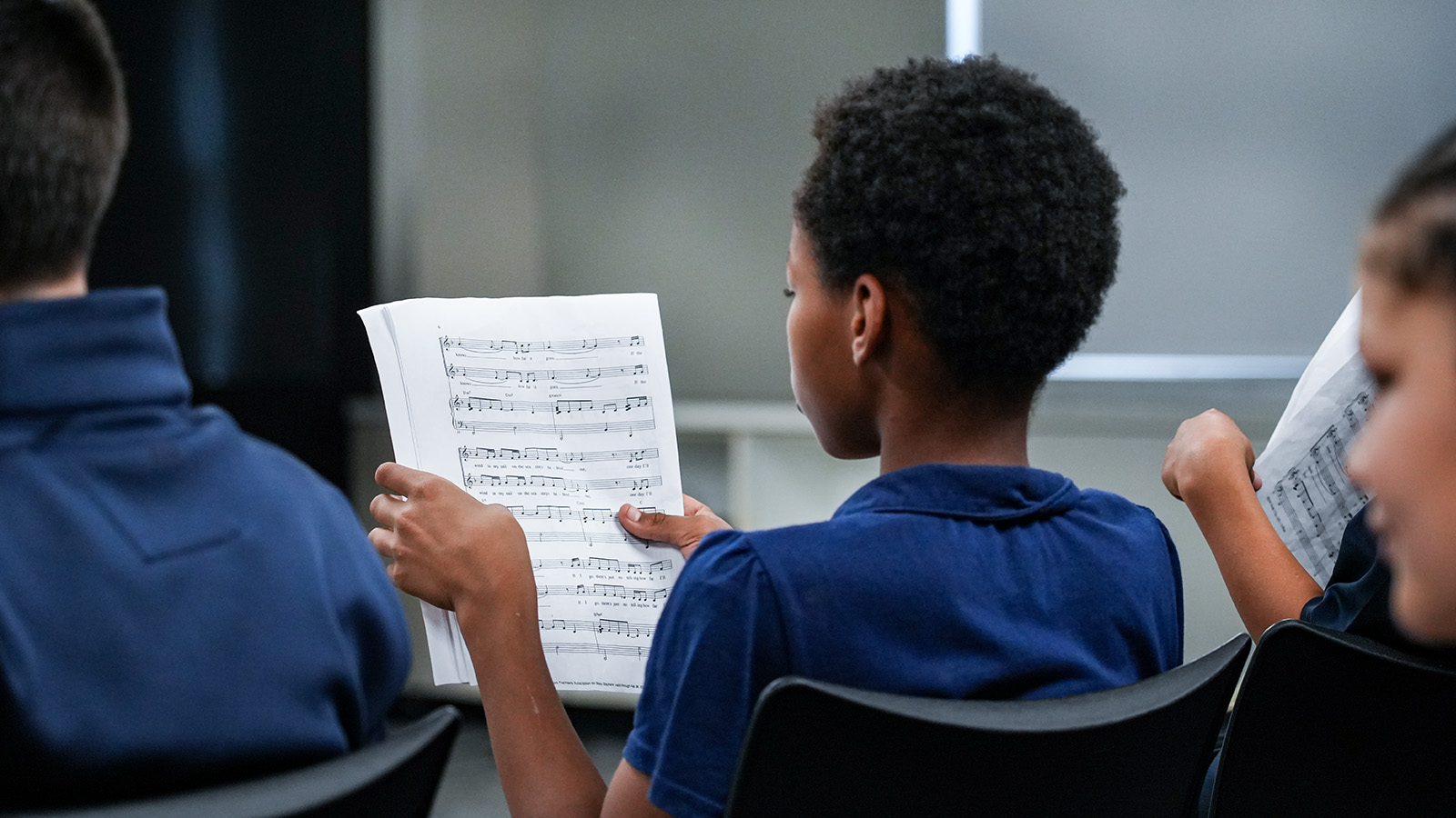 Paramount South Bend student holding sheet music while participating in a classroom music lesson with classmates