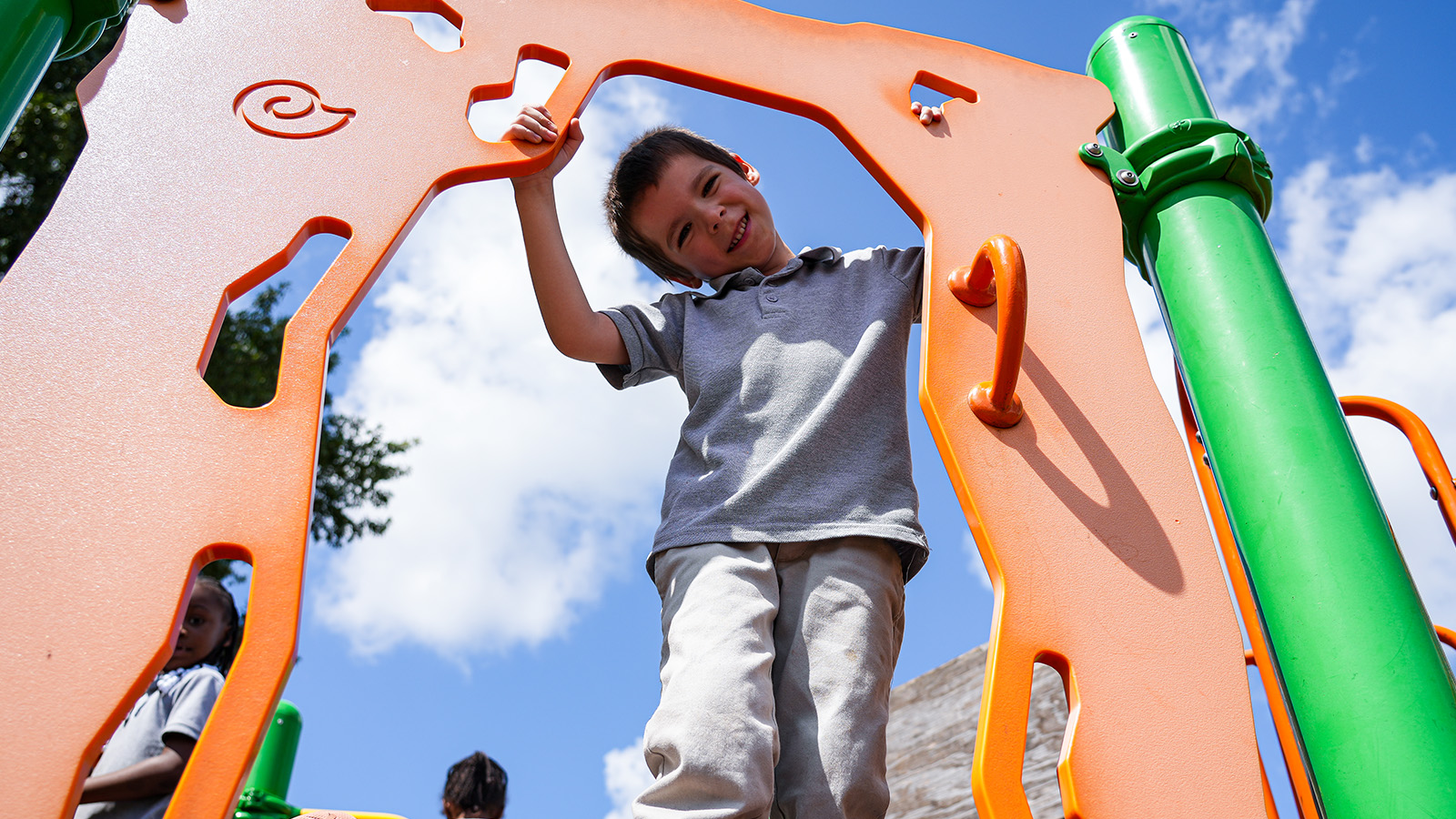 Paramount South Bend student smiling while climbing on colorful playground equipment outdoors
