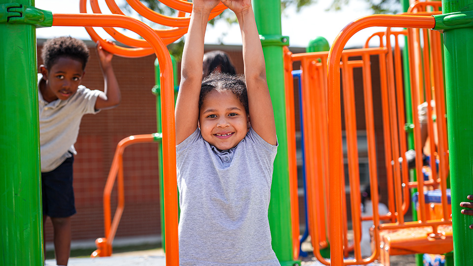 south-bend-parent-center-3 Smiling Paramount South Bend student hanging from overhead playground bars while classmates play nearby during outdoor recess